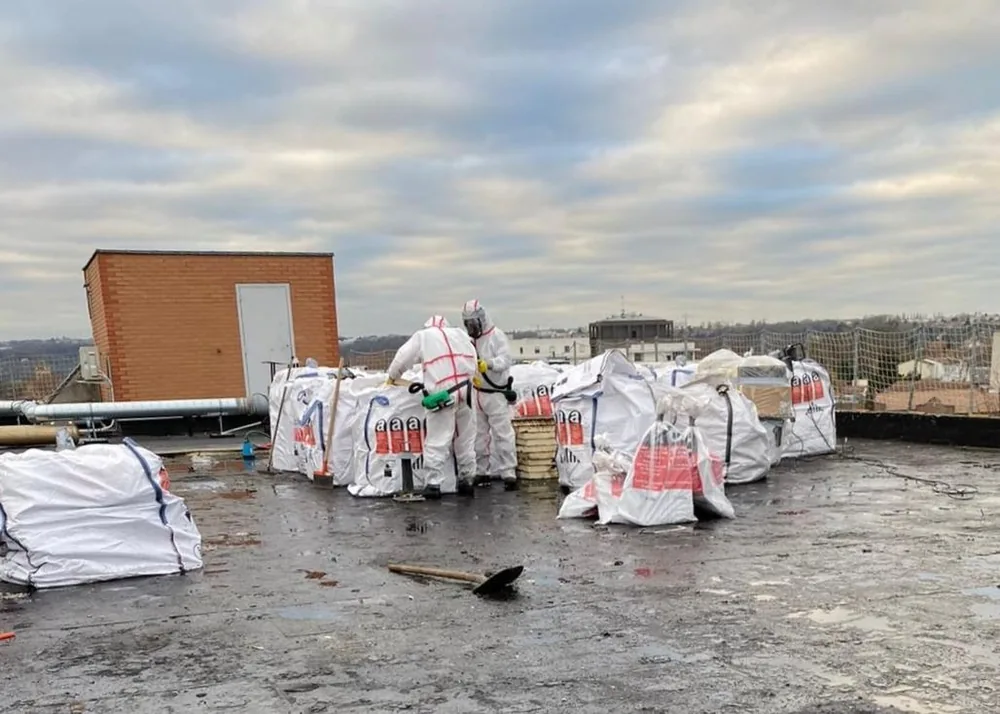 Opérateurs Delta.AP en combinaison conditionnant l'amiante en big bags sur une toiture-terrasse
